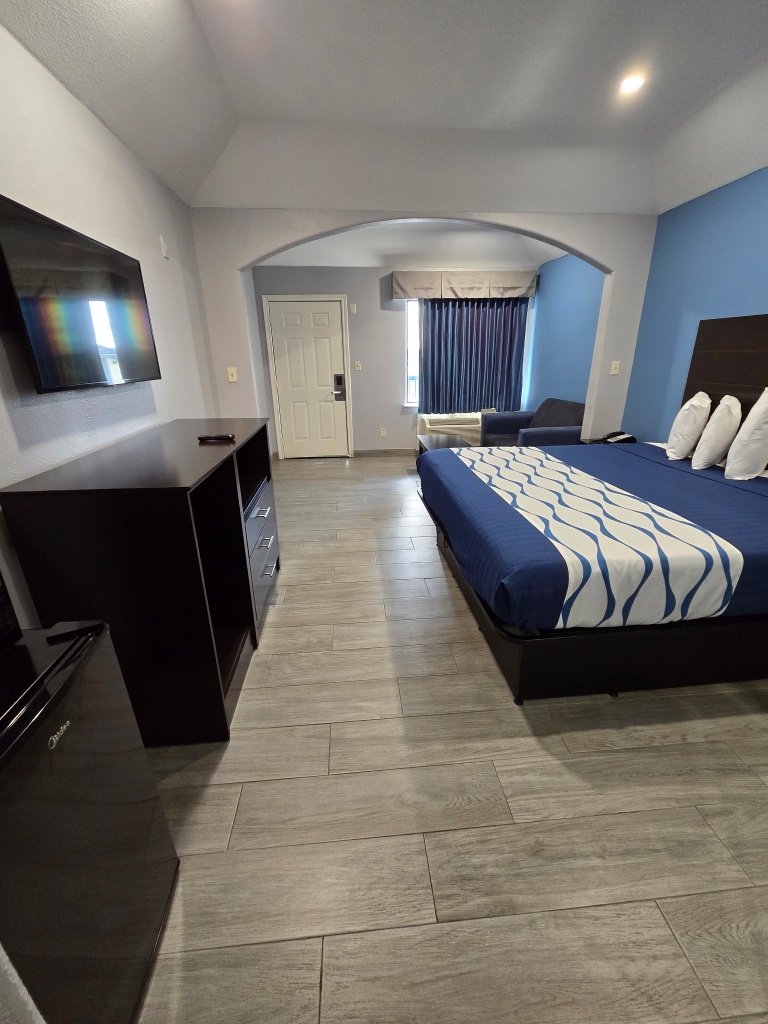 A hotel room with a blue and white bedspread, a black dresser, and a TV on the wall.