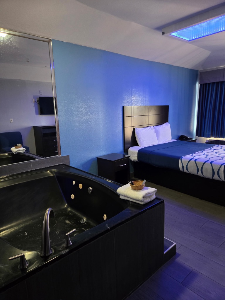 A hotel room with a large jacuzzi, king-sized bed, and mirror