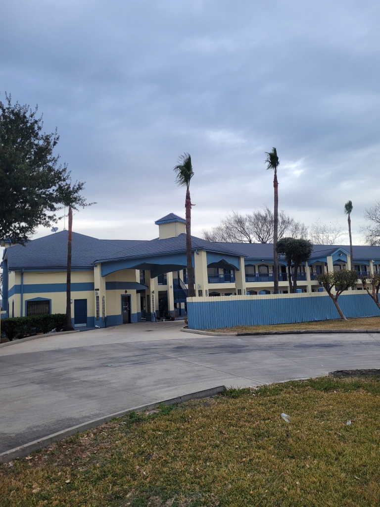 A two-story building with a blue and yellow exterior, a parking lot, and palm trees.