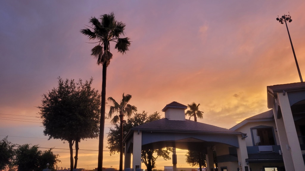 A building with a gazebo and palm trees in front of a sunset sky