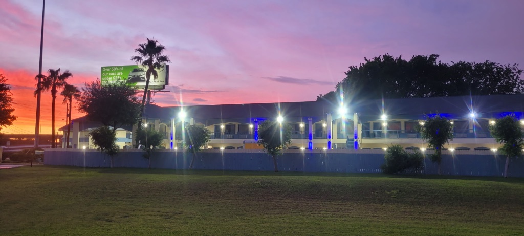 A two-story building with a flat roof and a grassy area in front of it at sunset.