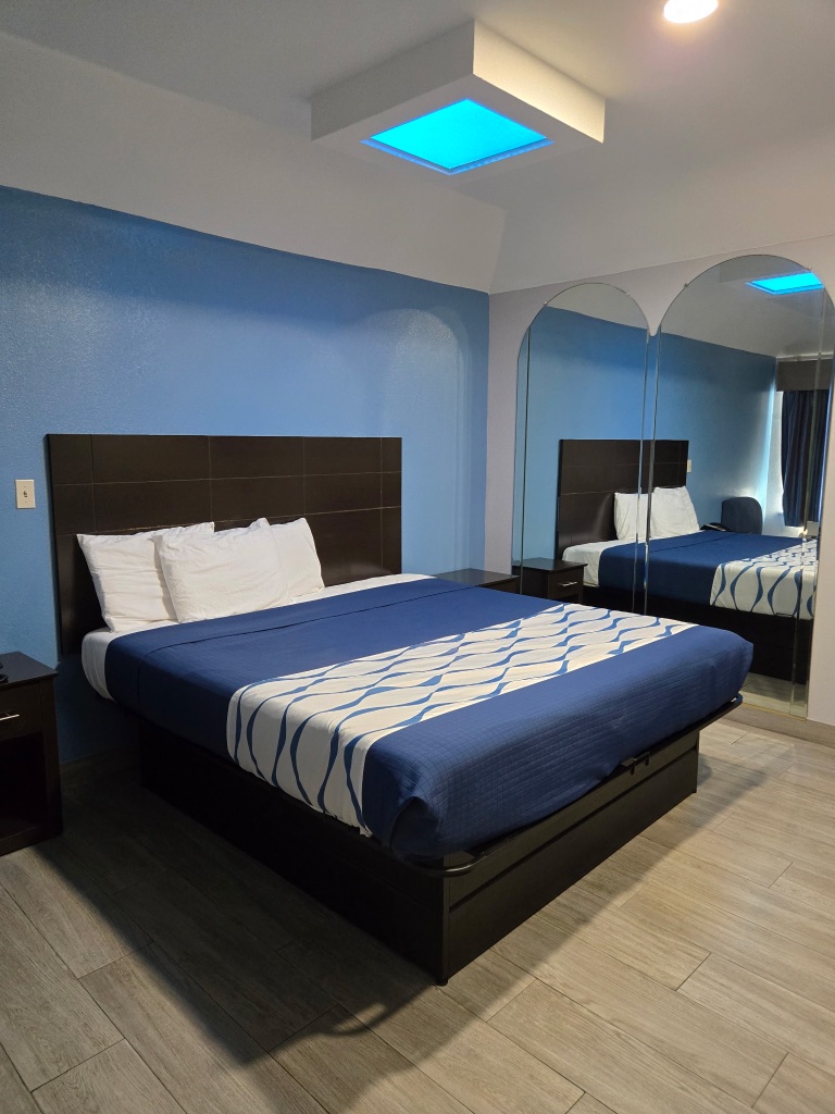 A hotel room with a bed, nightstand, and mirror