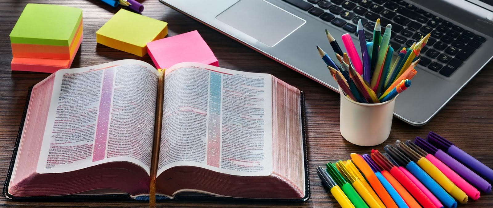 Open Bible surrounded by study notes, colored markers and a laptop