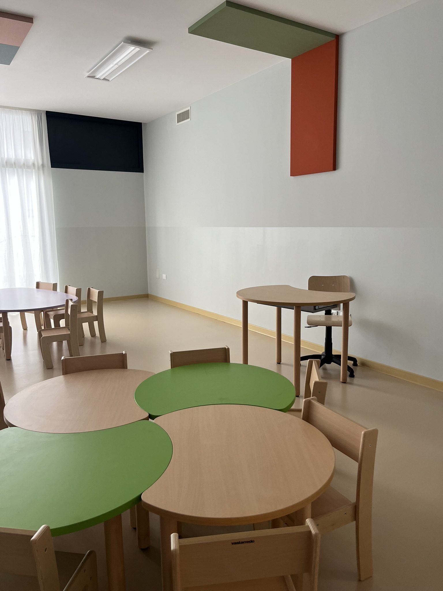Aula di una scuola dell'infanzia allestita con arredi scolastici in legno, tavoli circolari e pannelli acustici: esempio di fornitura conforme ai CAM arredi per interni del DM 23 giugno 2022