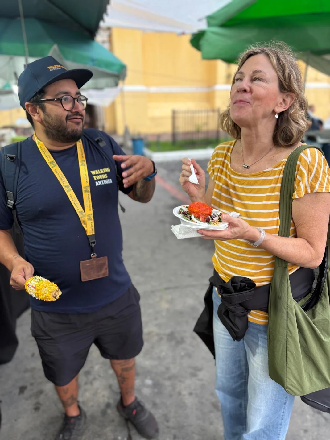 Guía y invitada disfrutando comida callejera bajo sombrillas del mercado
