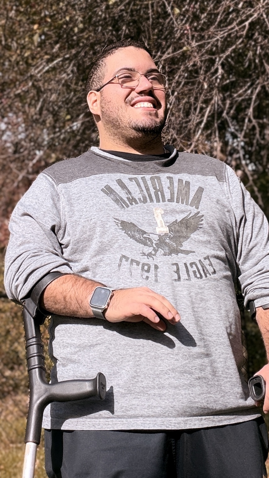 Smiling self-portrait in a grey sweater on crutches outdoors