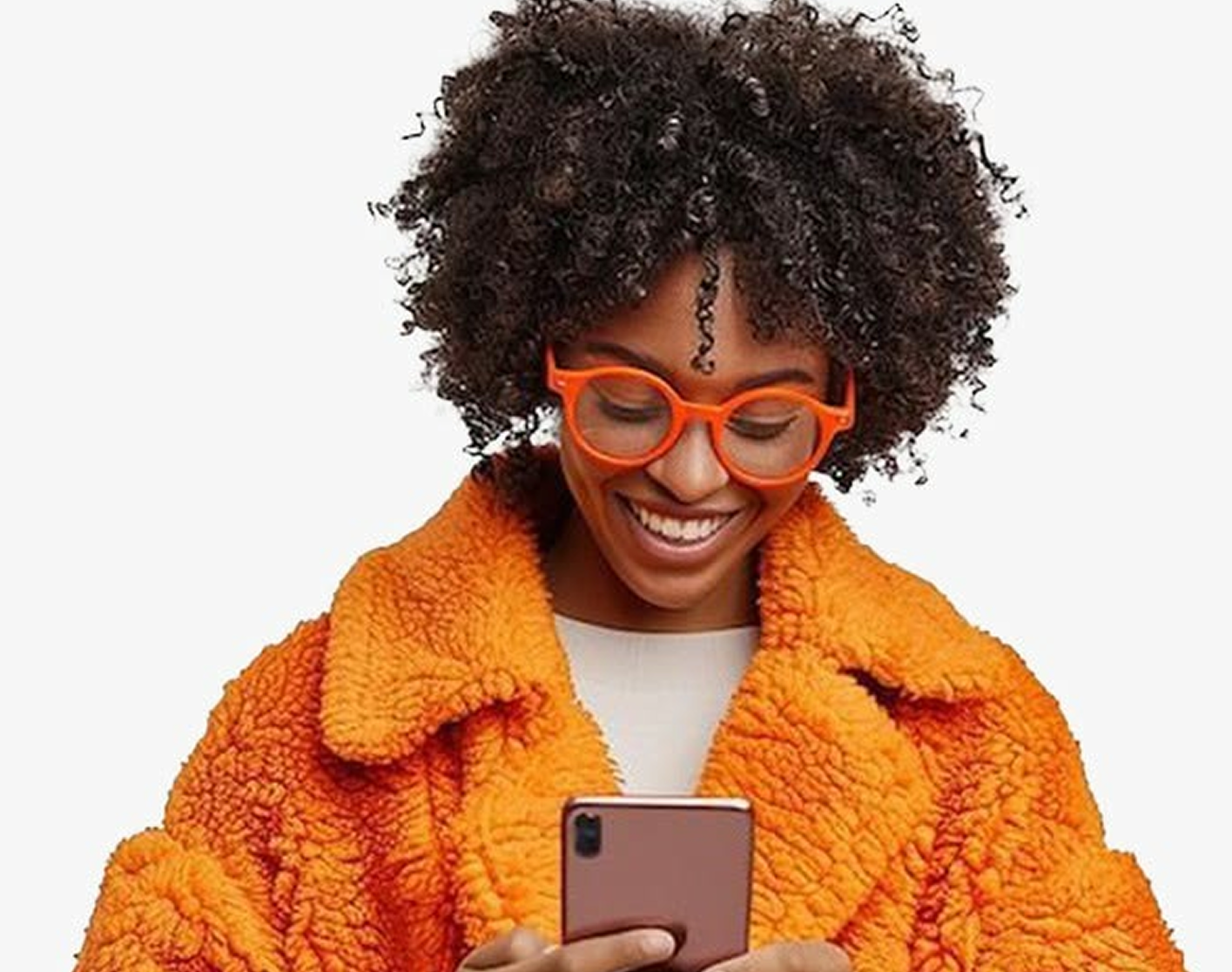 Woman with curly hair and orange glasses, wearing an orange coat and smiling at her phone