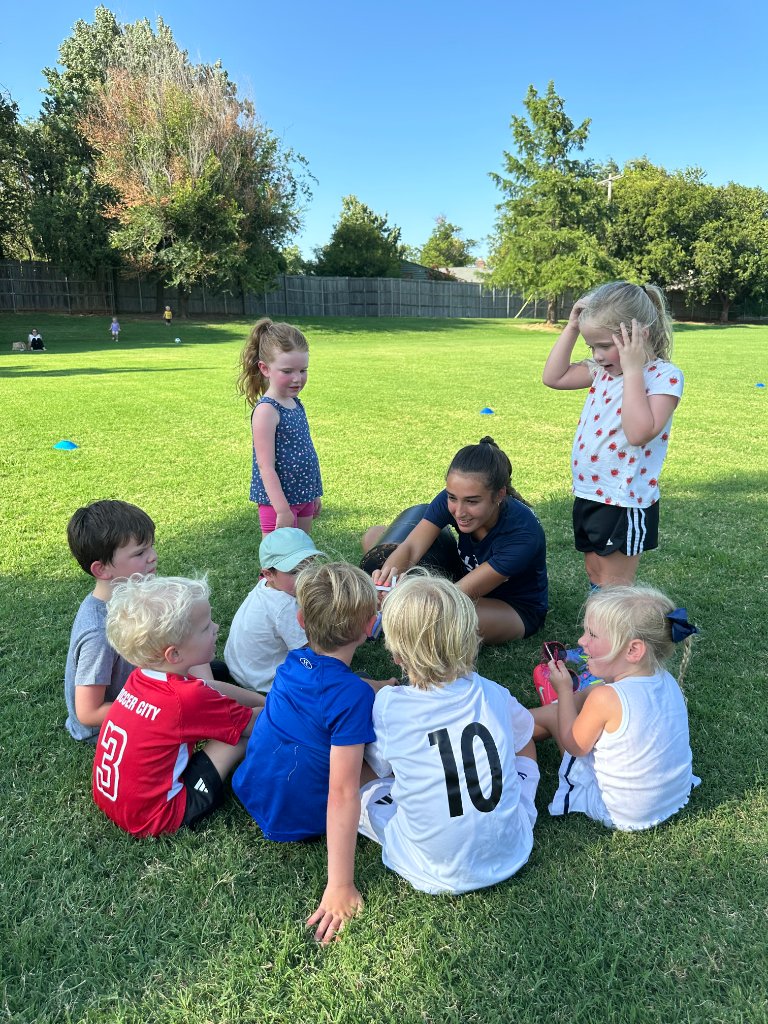 Children in prayer circle on a soccer field with a dove above