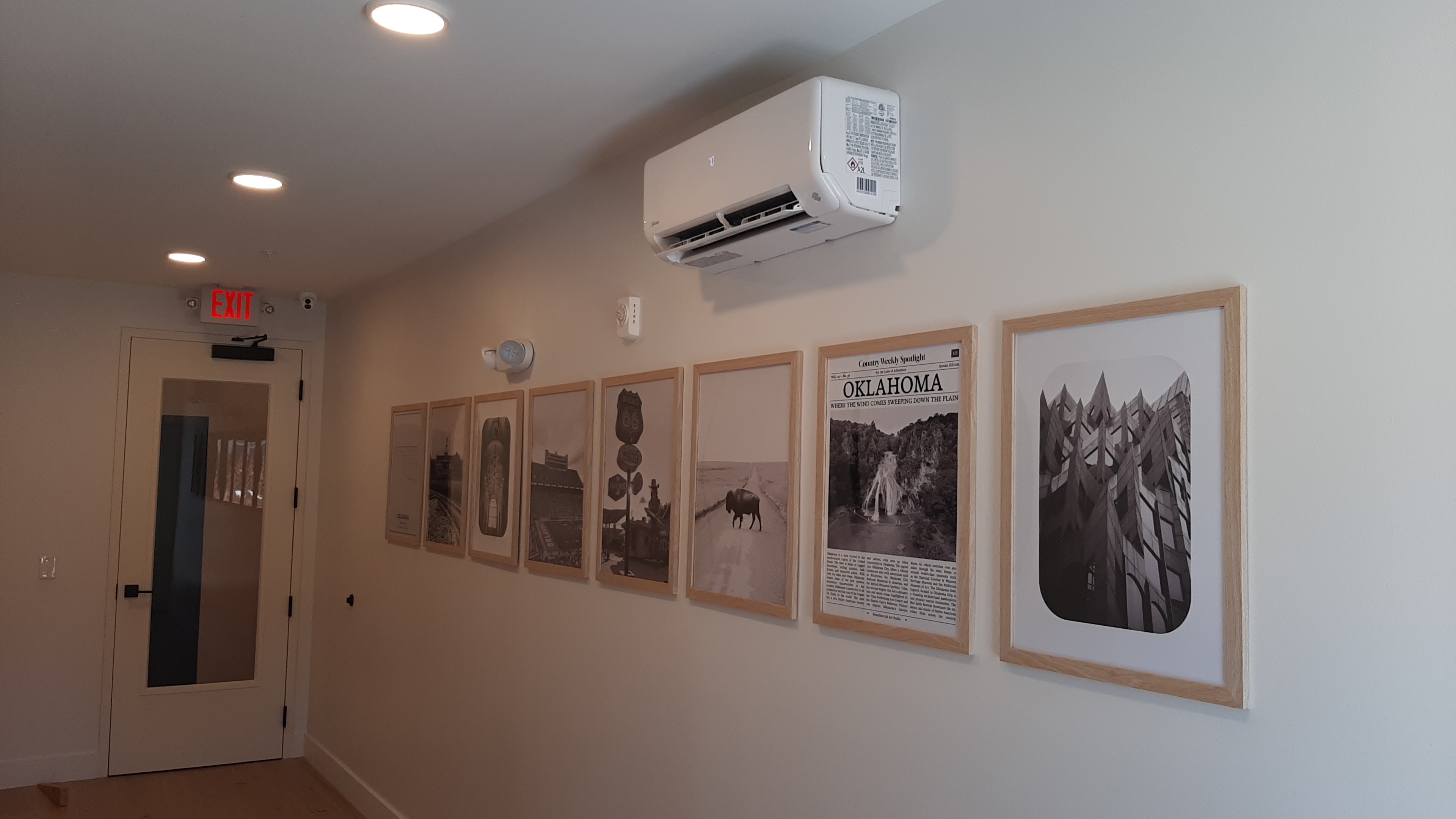 Oklahoma-Themed Hallway Gallery Wall in Edmond, OK | Redhawk Handyman Row of Oklahoma-themed framed prints, including vintage newspaper artwork, installed in an evenly spaced gallery wall along a resident hallway in a new Edmond, OK apartment building