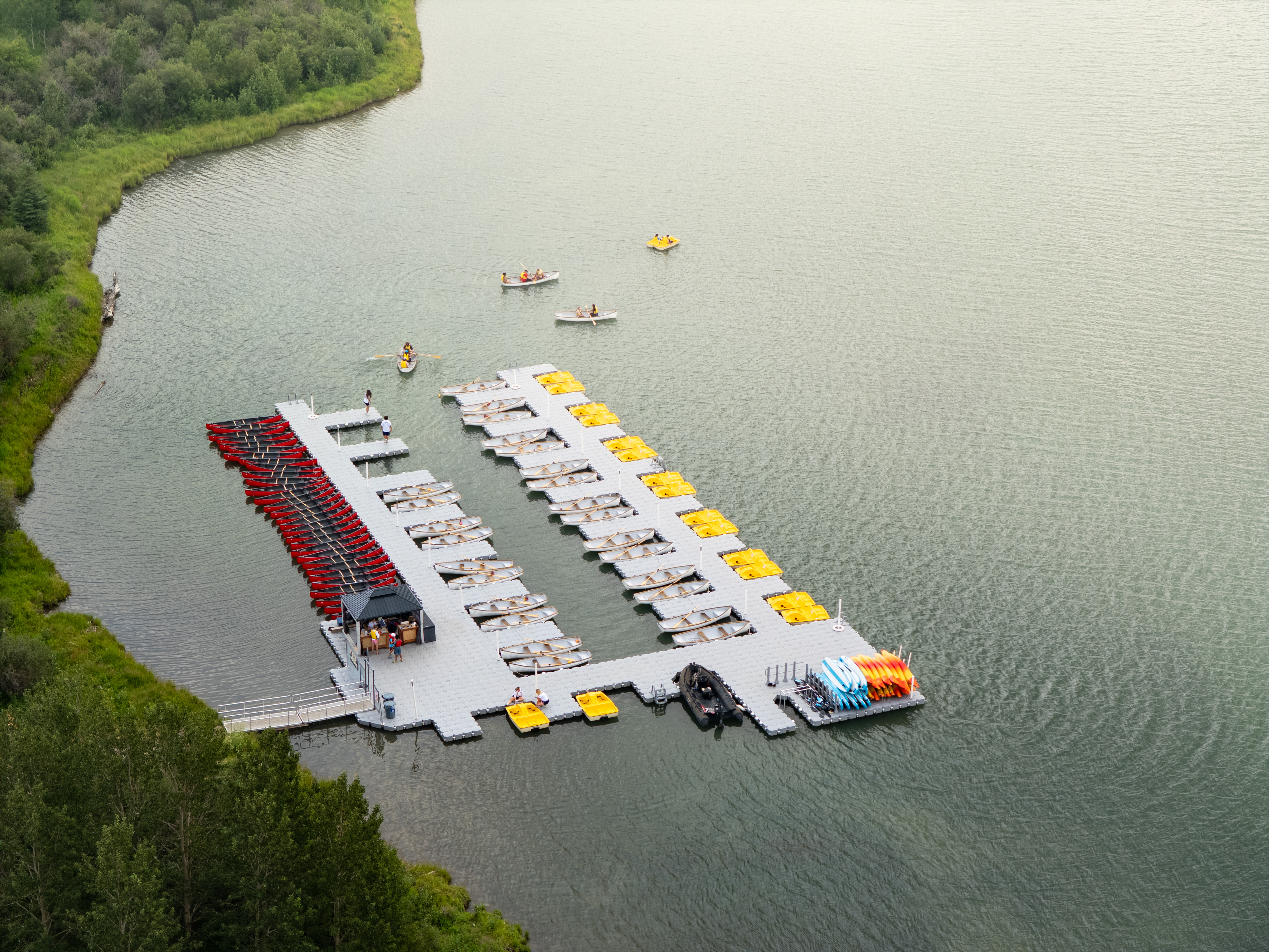 Aerial view of Bearspaw Marina's rental dock on Bearspaw Reservoir — boats out on the water and a fleet of canoes, kayaks, and pedal boats at the floating dock