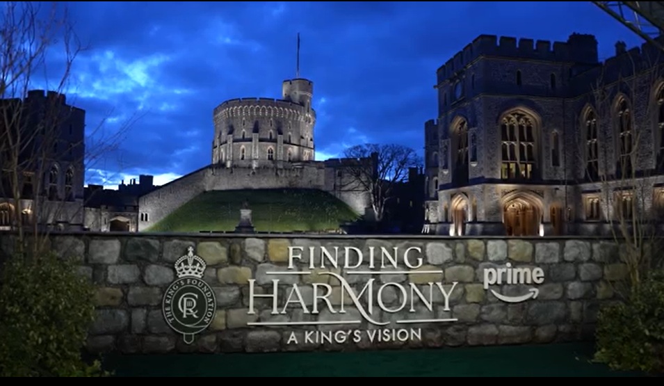 Windsor Castle at dusk with a sign for Finding Harmony: A King’s Vision mounted on the garden wall.