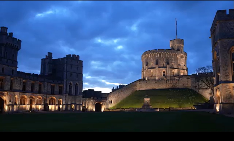 Windsor Castle illuminated against a deep blue dusk sky, with the Round Tower rising above the ramparts.