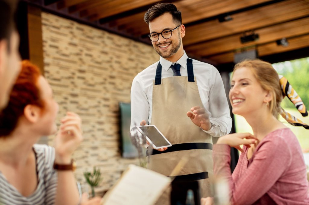 Waiter using digital tablet with happy customers