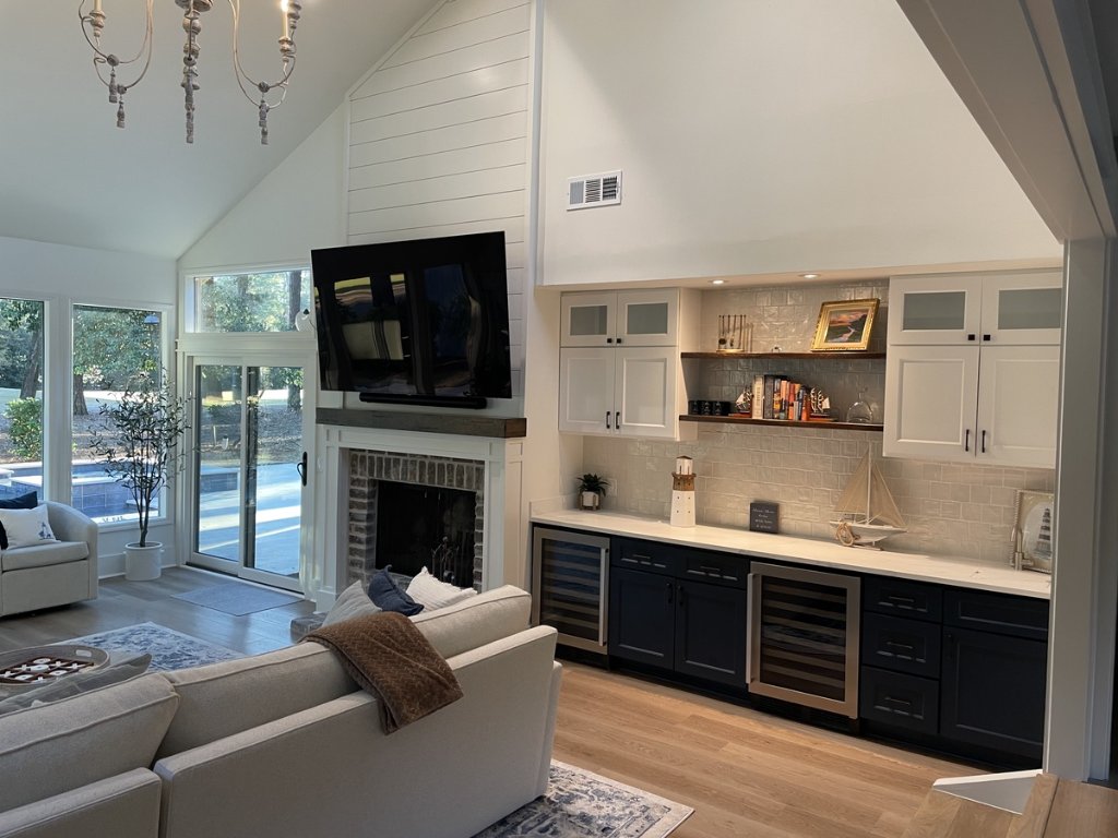 Modern luxury living room with cathedral ceilings, shiplap accent wall, custom wine bar cabinetry, updated fireplace, hardwood floors, and pool view after Blueprint Construction remodel — Golden Isles, GA