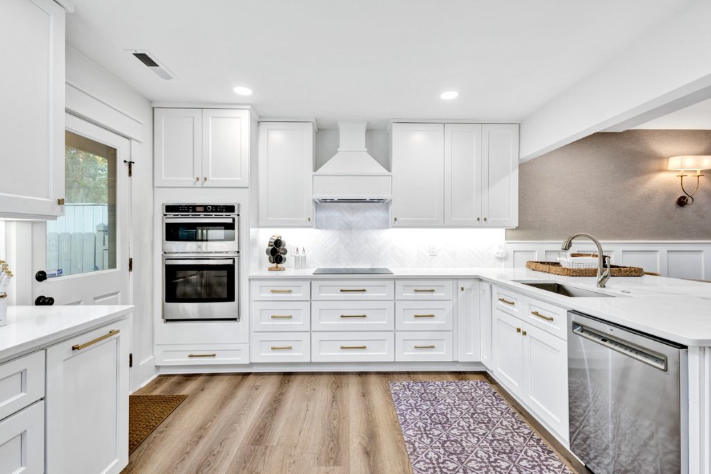 Luxury modern kitchen with white cabinetry, marble backsplash, stainless steel appliances, brass hardware, and wood flooring after Blueprint Construction remodel — Golden Isles, GA