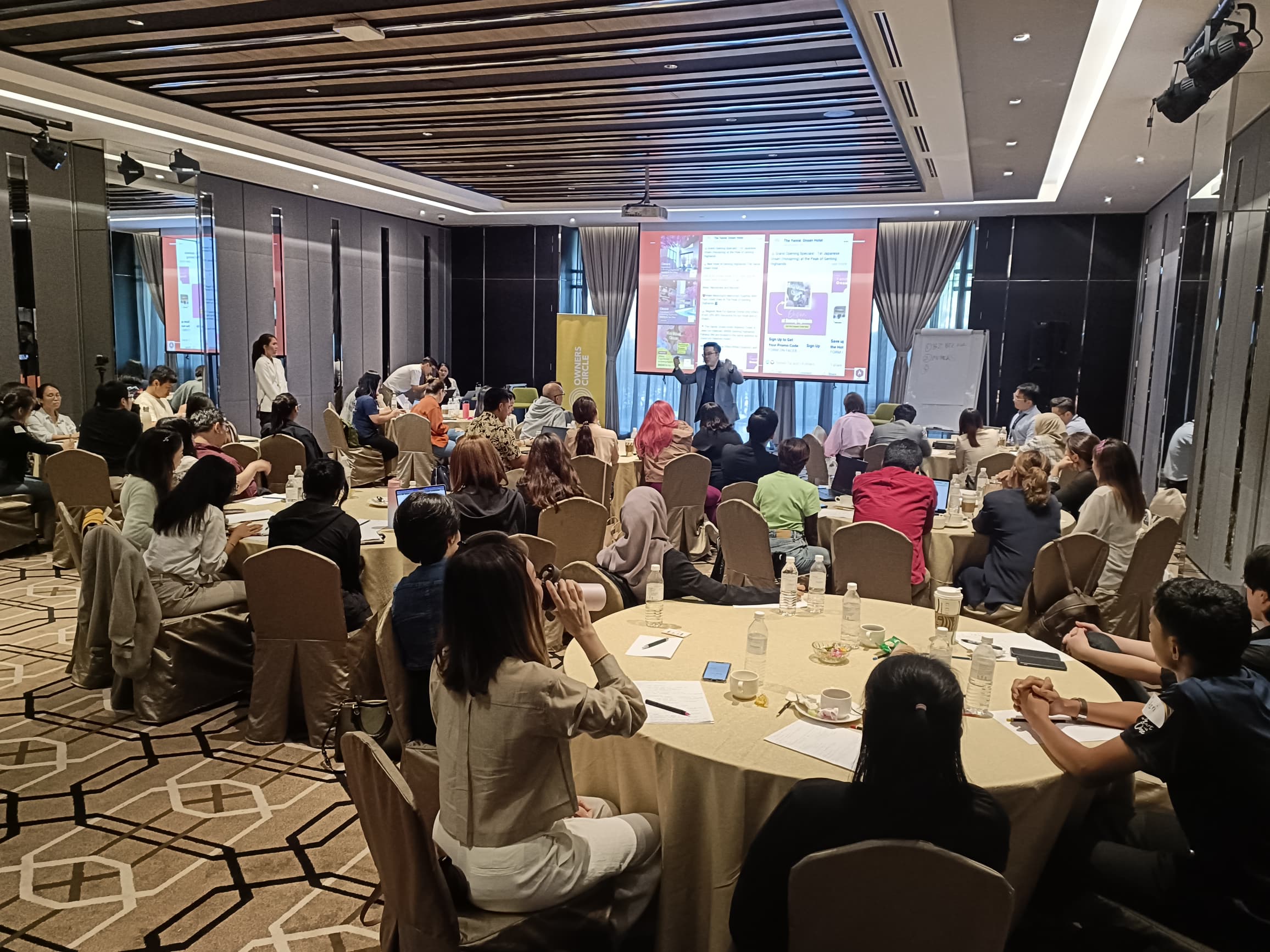 Eli Hong presenting at an Owners Circle conference with round-table seating