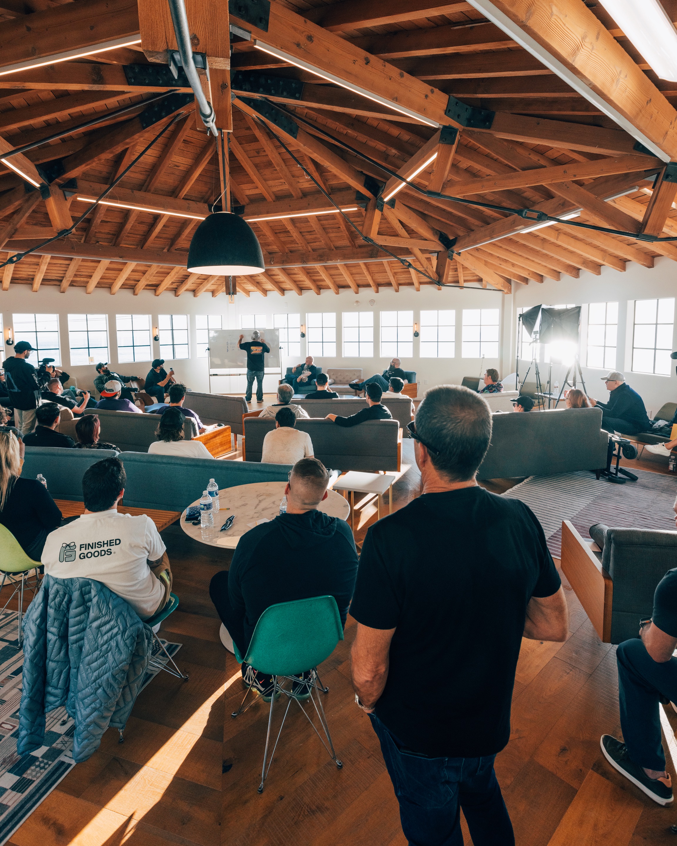 An audience gathered around a standing speaker in a wood-beam event room