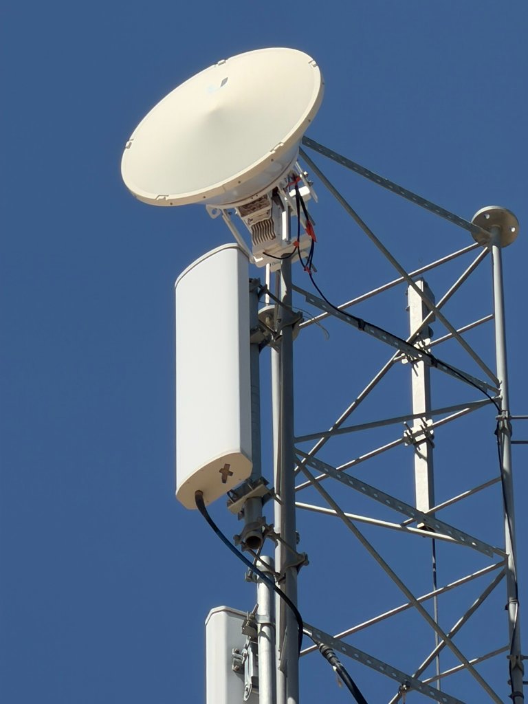 Microwave dish and panel antennas precision-mounted on a lattice tower, showing cabling and mounting brackets against blue sky