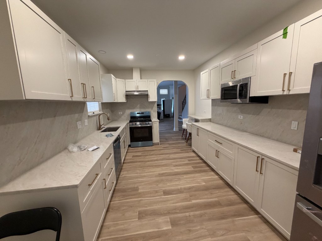 Bright white shaker kitchen with marble backsplash and gold hardware by Remodeling Kings
