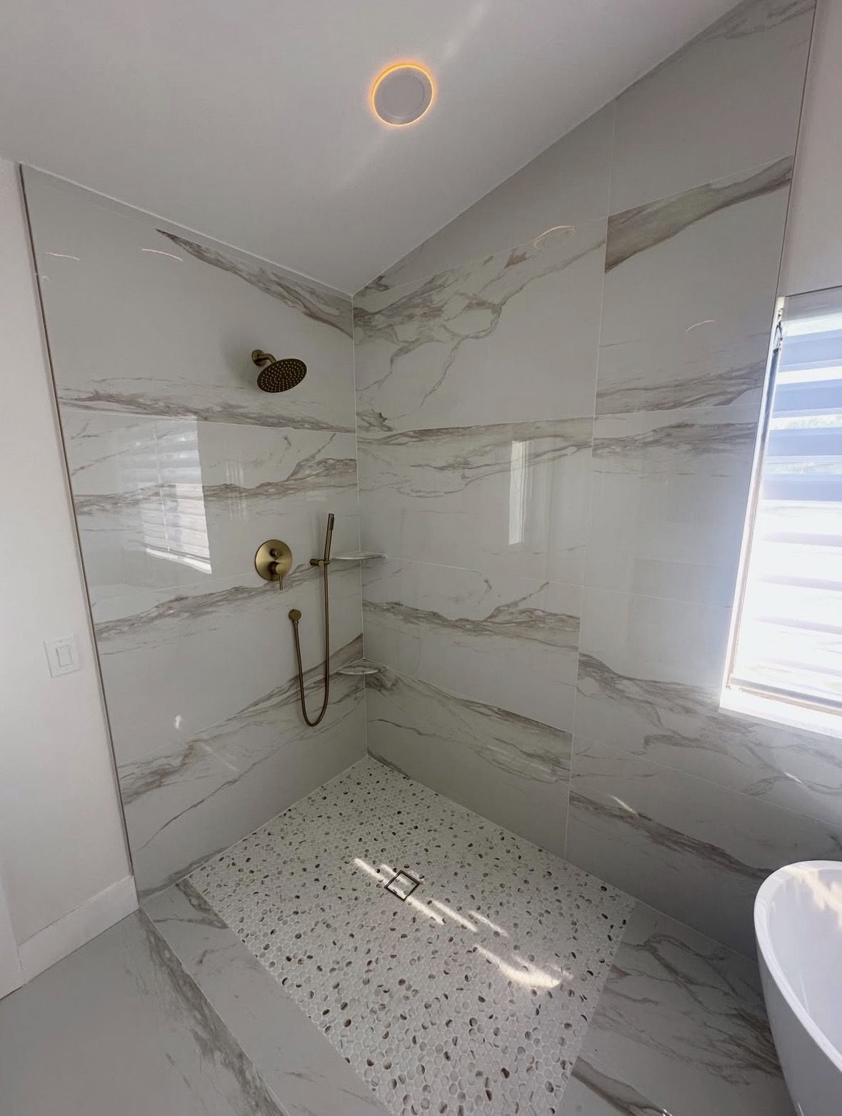 Walk-in shower detail from a bathroom remodel in Hinsdale, IL — pebble mosaic floor and brushed-gold shower system