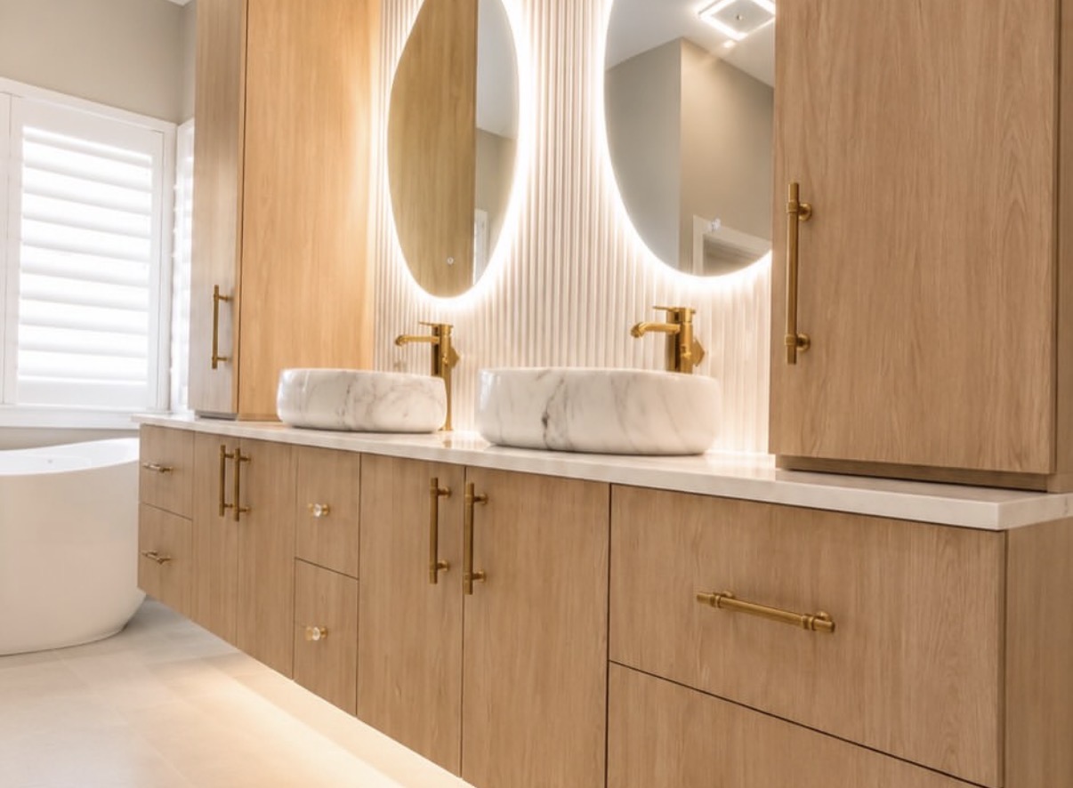 Angled view of a floating double vanity with tall storage towers, vessel sinks, and backlit mirrors on a fluted panel wall