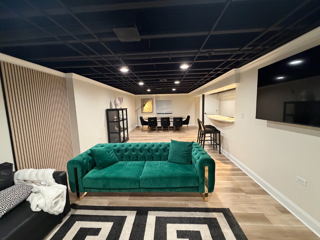 Modern lounge basement with black ceiling, bar nook, and wood slat accent walls by Remodeling Kings