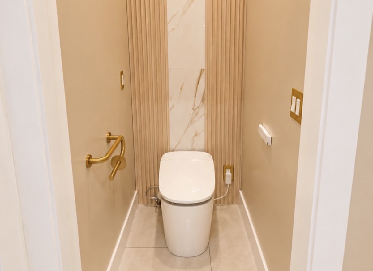 Private toilet alcove with fluted wall panels, marble center insert, and brushed-gold grab bar and toilet paper holder