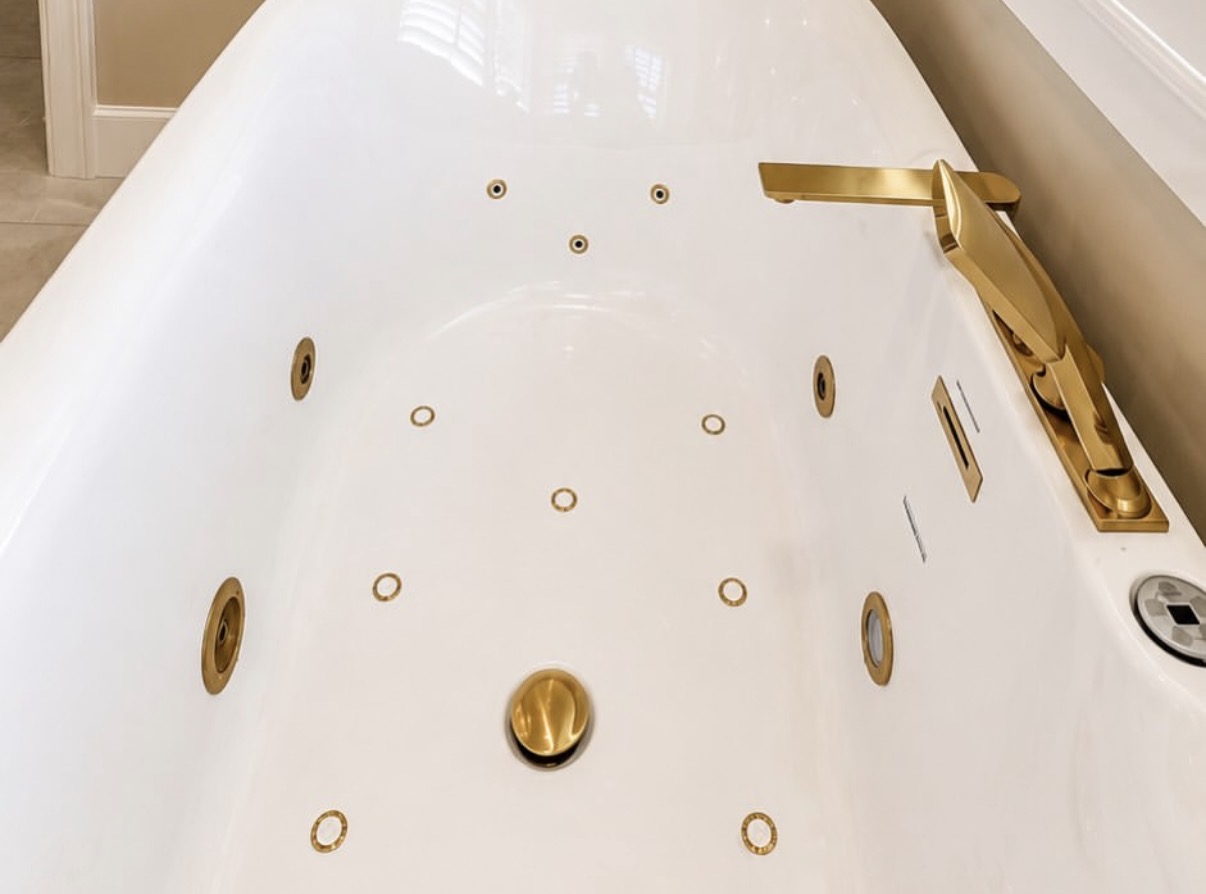 Detail of a white jetted bathtub with brushed-gold jets, drain, and deck-mounted faucet