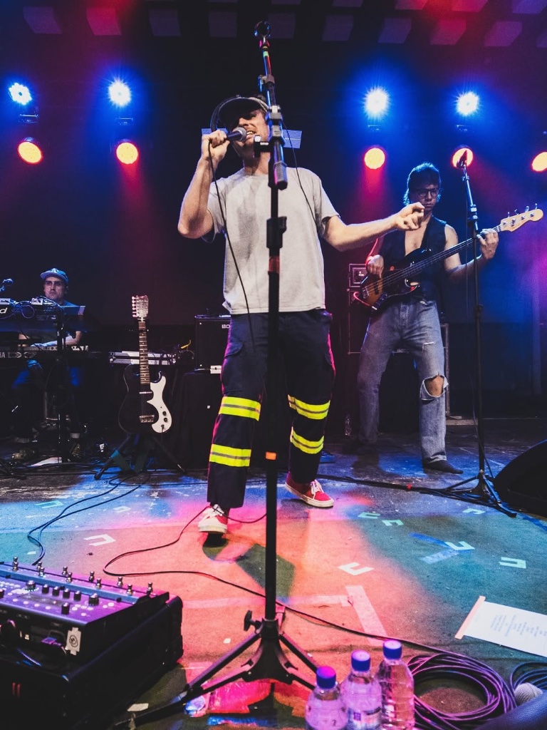 Mac DeMarco and full band on stage under red, blue and purple lights