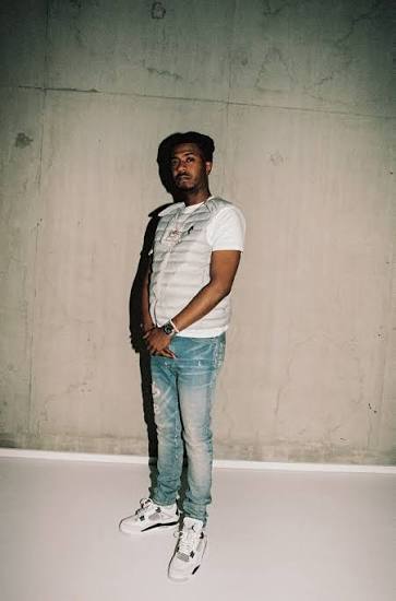 Nines in a quilted puffer vest and light-wash jeans, photographed in a minimalist studio environment.