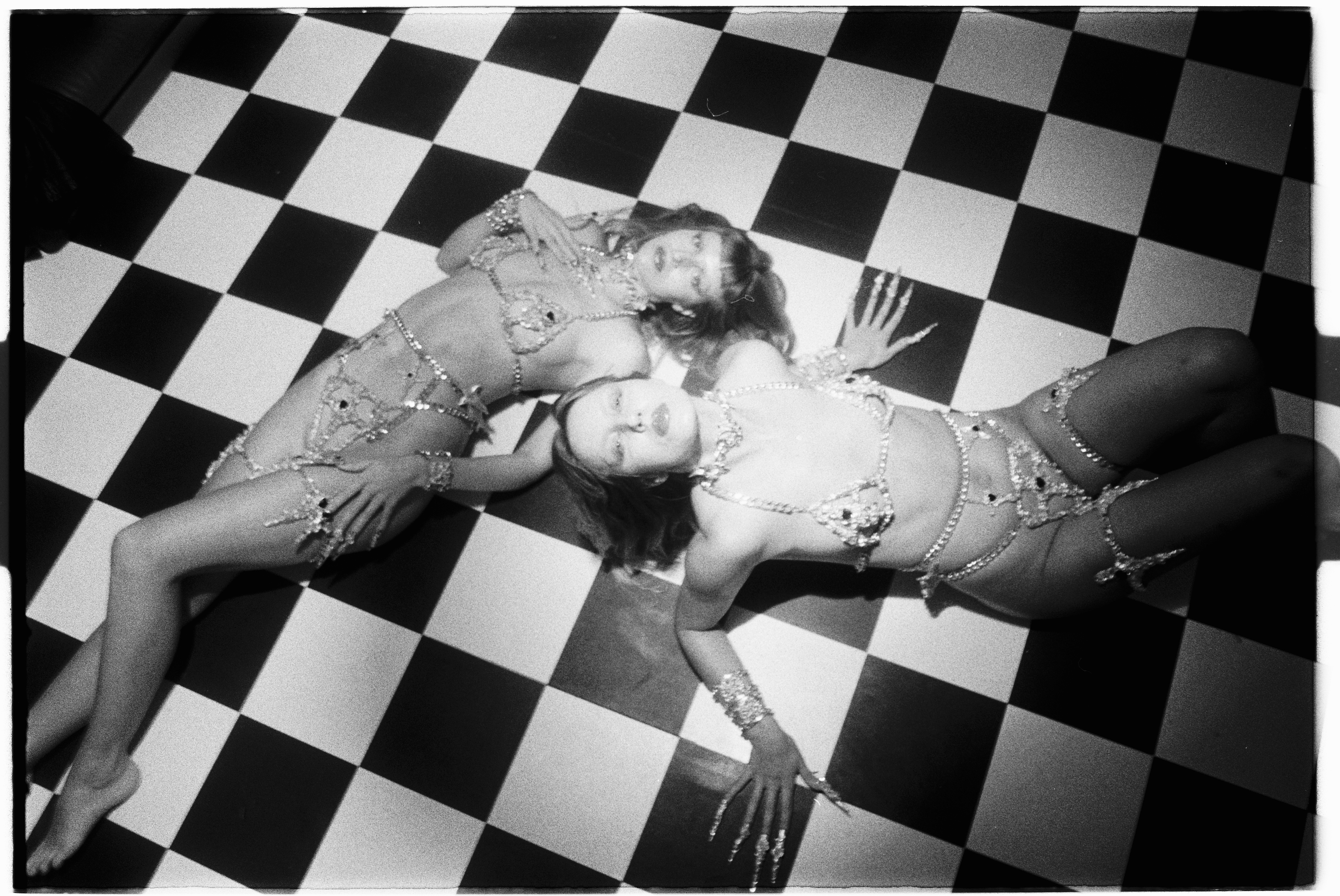 MOTHERMARY twins lying on checkerboard floor in jeweled body chains, black and white film photograph