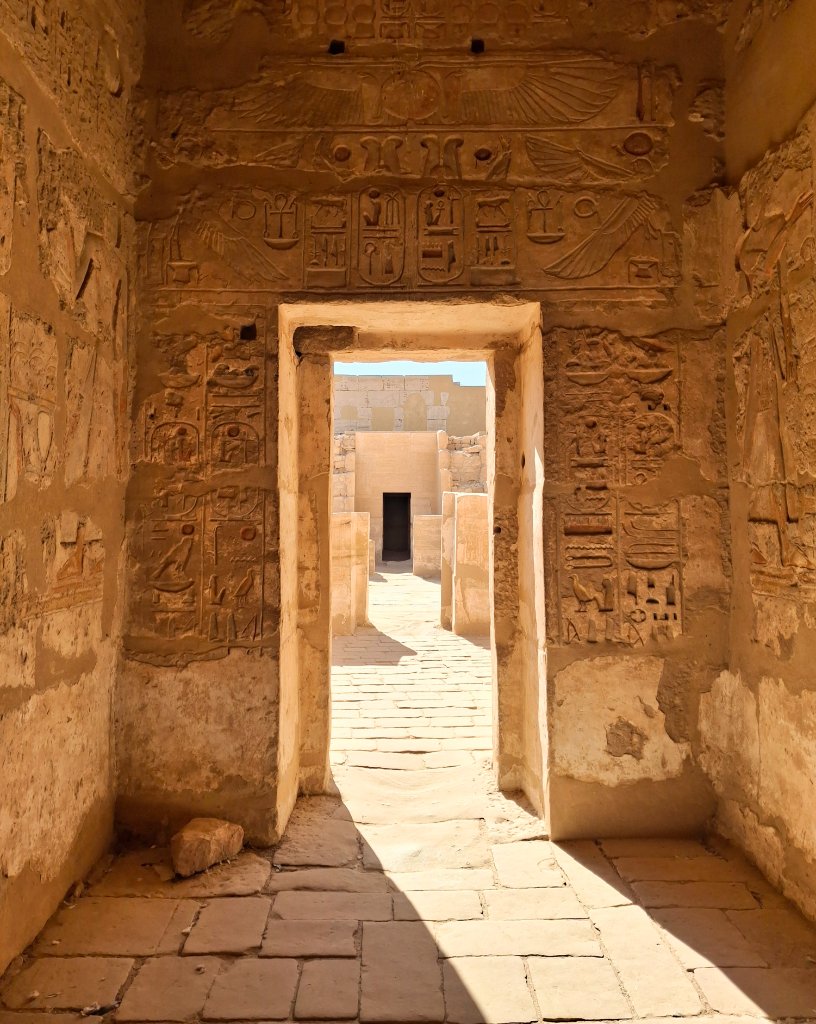 Ancient Egyptian temple doorway with hieroglyphic carvings leading to a sunlit corridor
