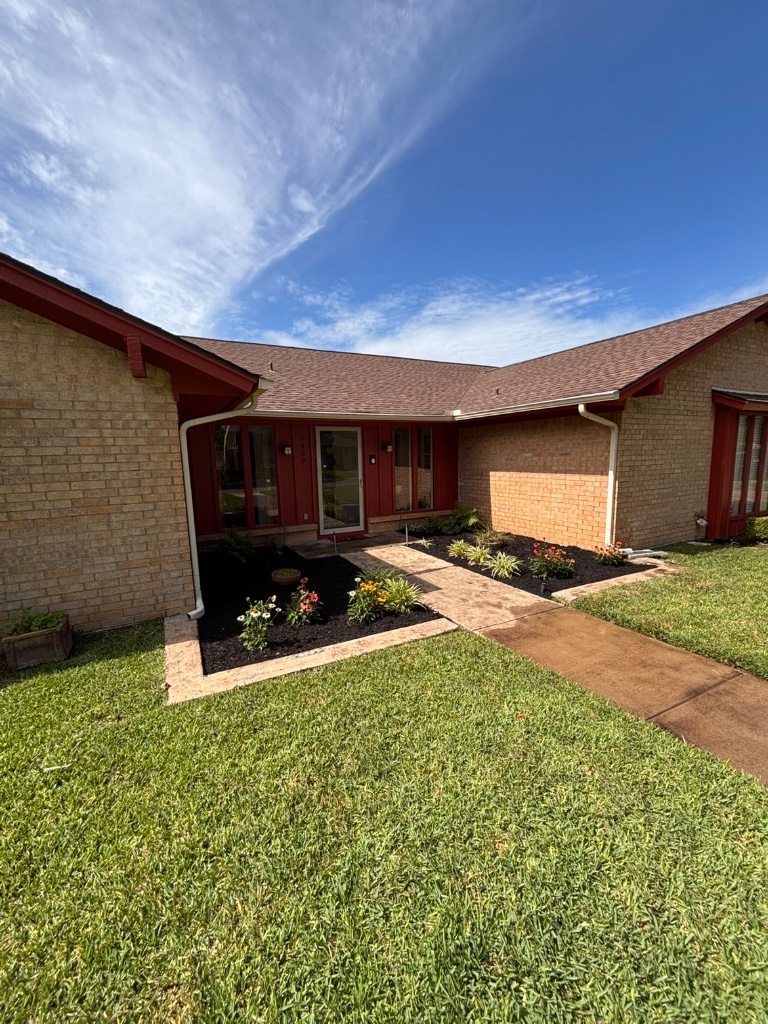 Flowerbed installation in Arlington TX — fresh black mulch, seasonal flowers, and a manicured green lawn in front of a brick home