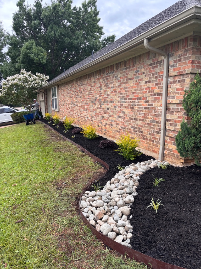 Curved flowerbed with steel edging river rock and lime shrubs installed in Arlington TX