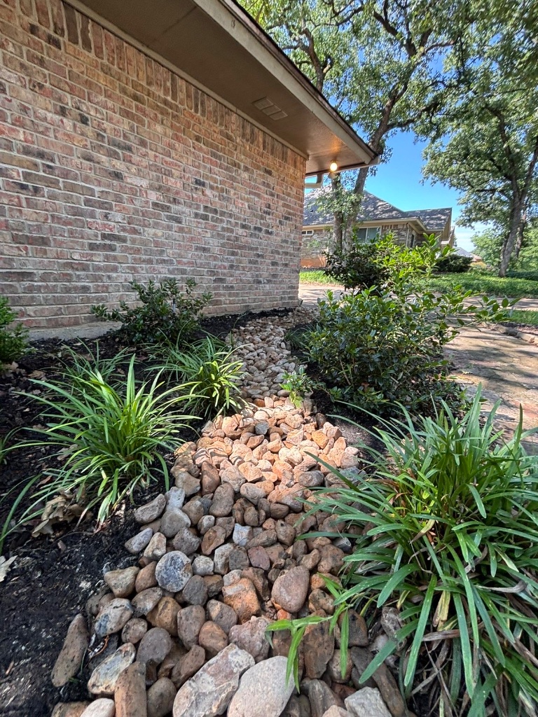 River rock drainage dry creek bed installation with mulch and grasses alongside a brick home in Arlington TX