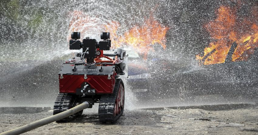 A tracked firefighting robot operating near a vehicle fire with water spray