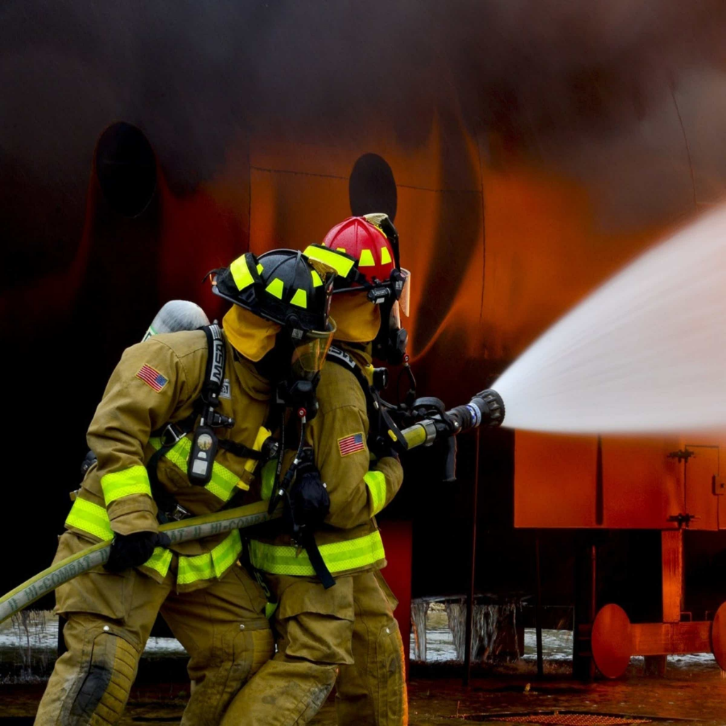 Two firefighters in full turnout gear operating a hoseline at a training burn