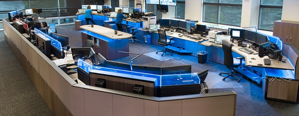 A modern 911 dispatch center with multiple workstations and large display screens