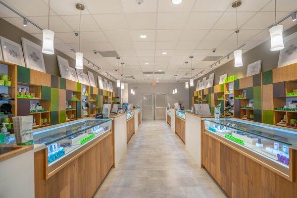 A long central aisle inside a Trulieve dispensary, with service counters, backlit wood shelving and pendant lighting.
