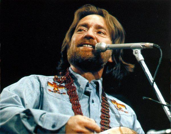 Willie Nelson performing on stage in a blue shirt