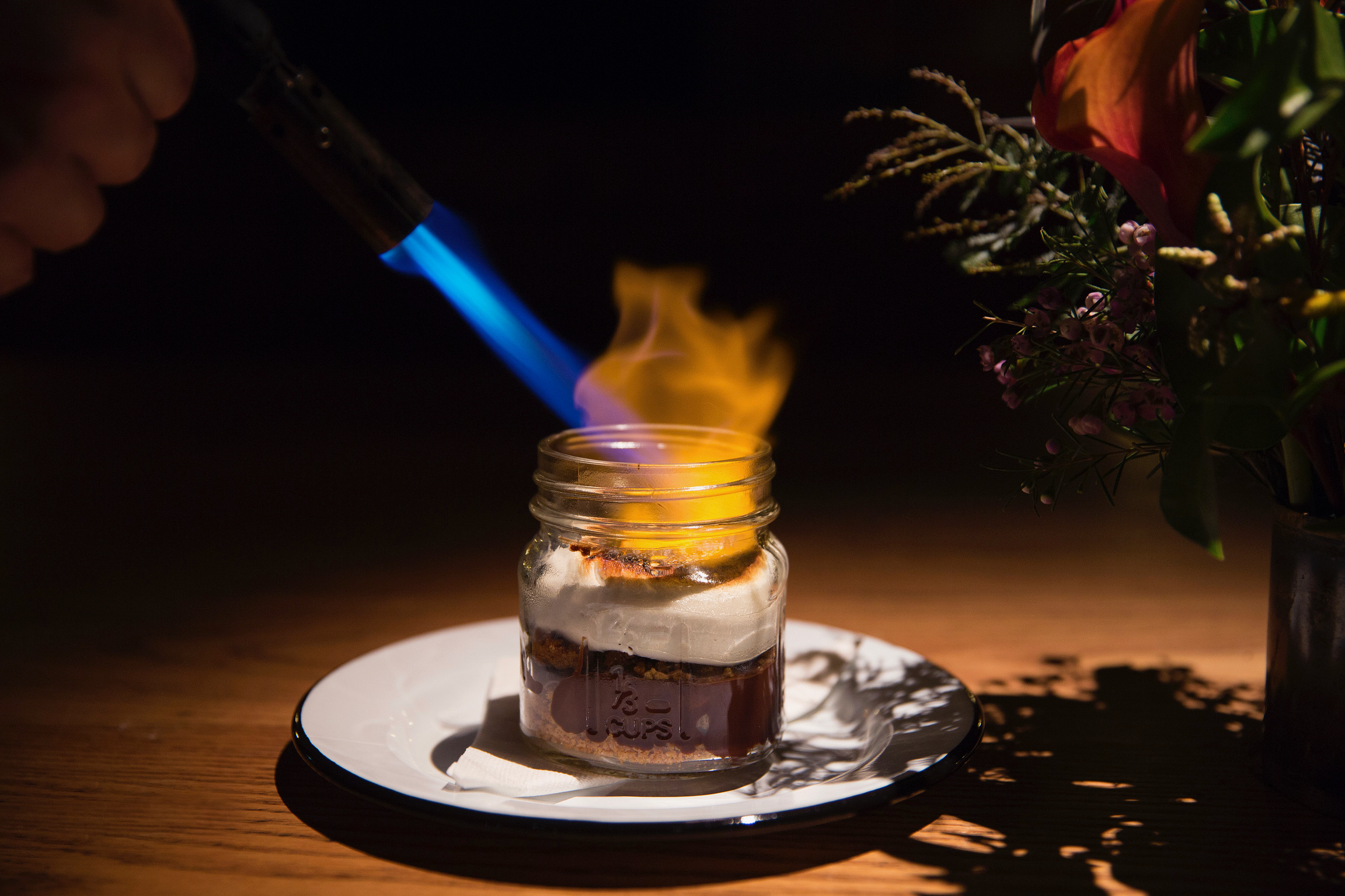 Kitchen torch caramelizing a marshmallow atop a s'mores dessert in a mason jar