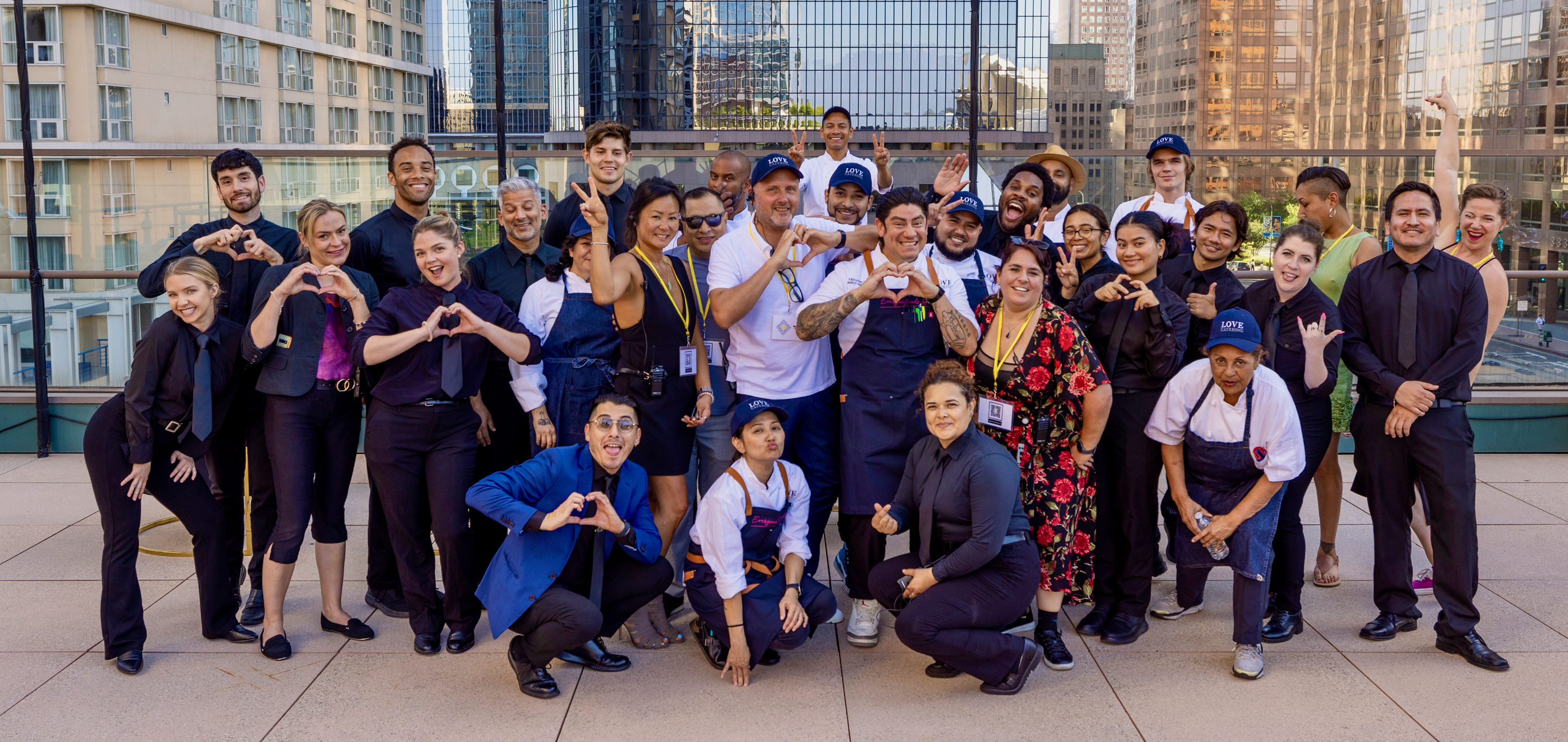 The Love Catering team posing together on a rooftop terrace in Los Angeles, wearing black uniforms and branded caps