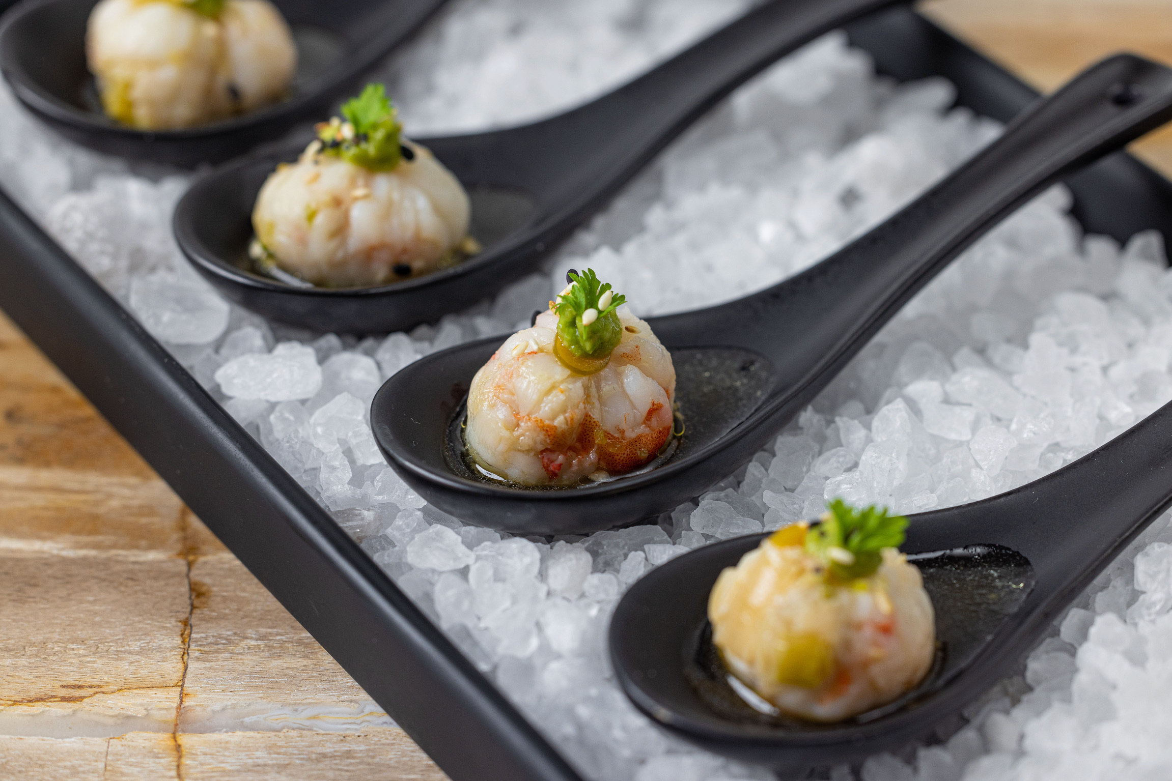 Four seafood appetizers on black ceramic spoons nestled in a bed of coarse sea salt
