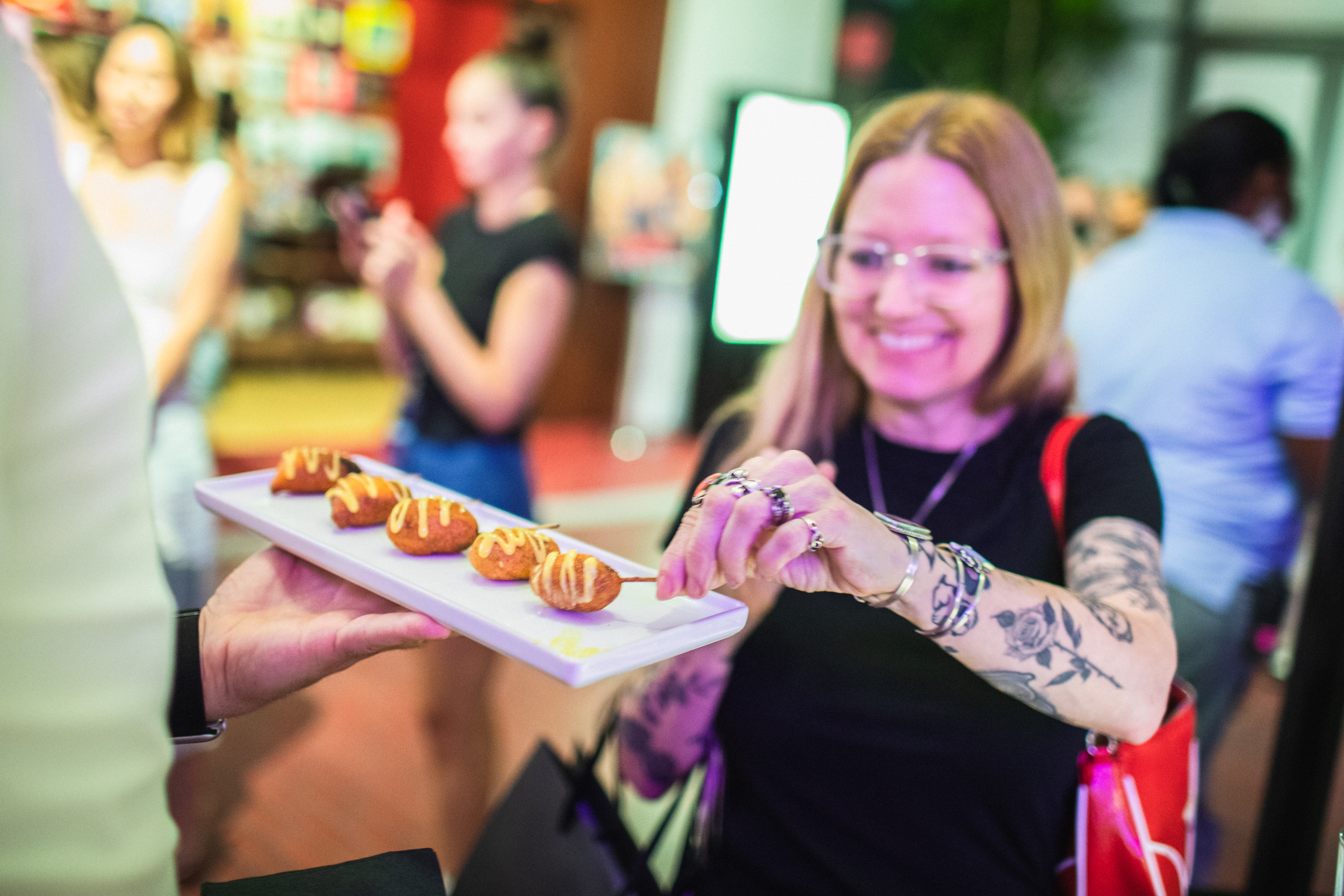 Catering server offering a platter of golden skewered bites to a smiling guest at an event