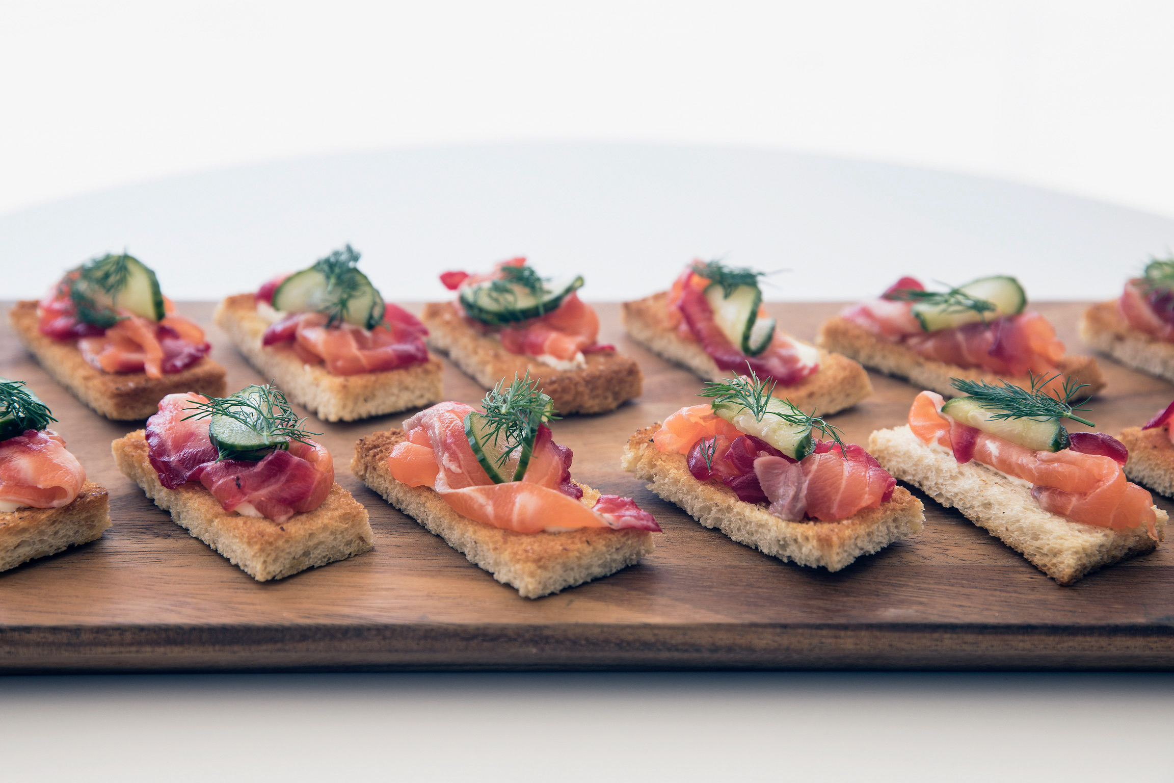 Twelve cured salmon and dill crostini arranged on a wooden serving board