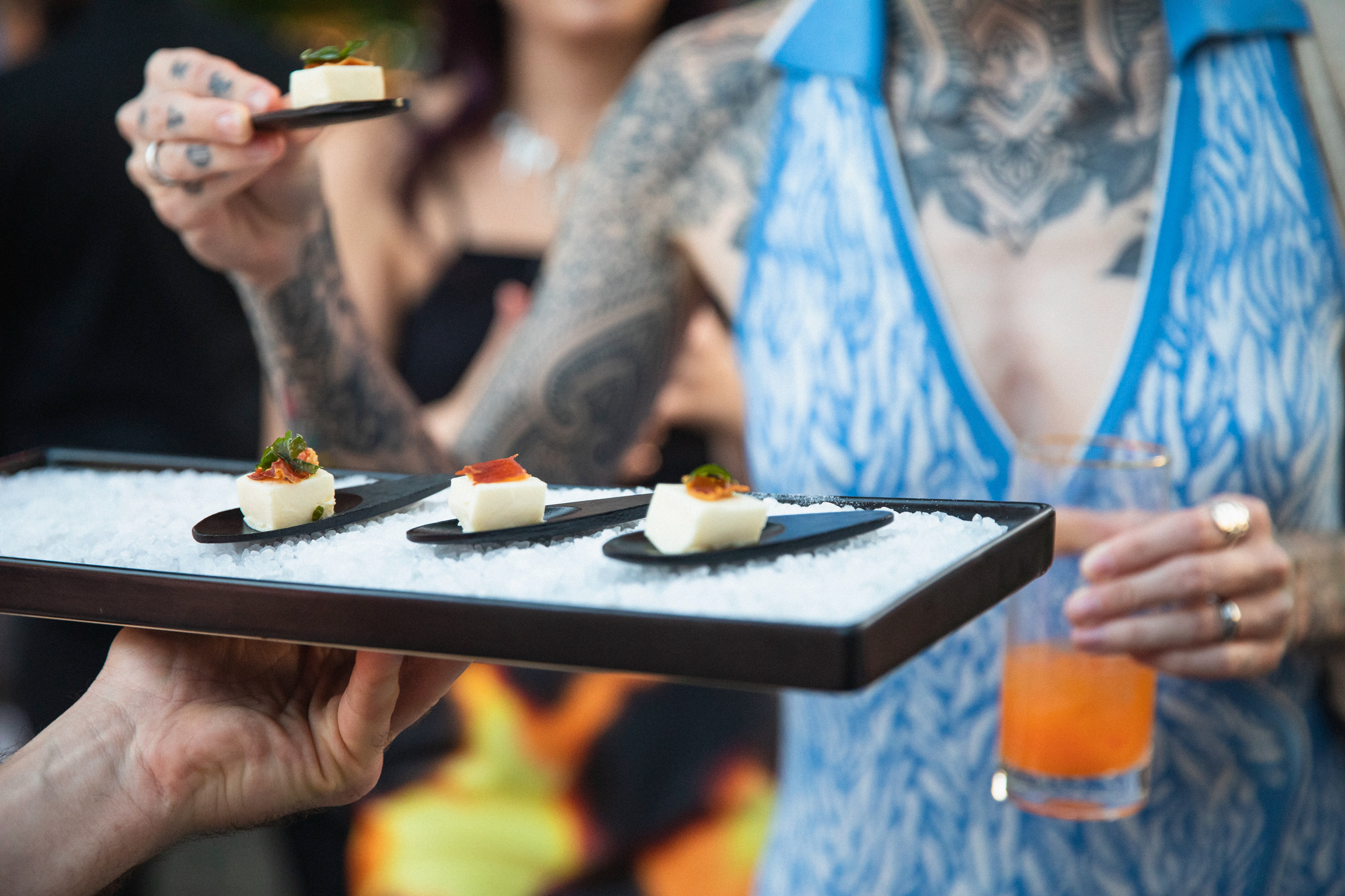Hand holding a black salt-bed tray of cured meat and white bites on tasting spoons