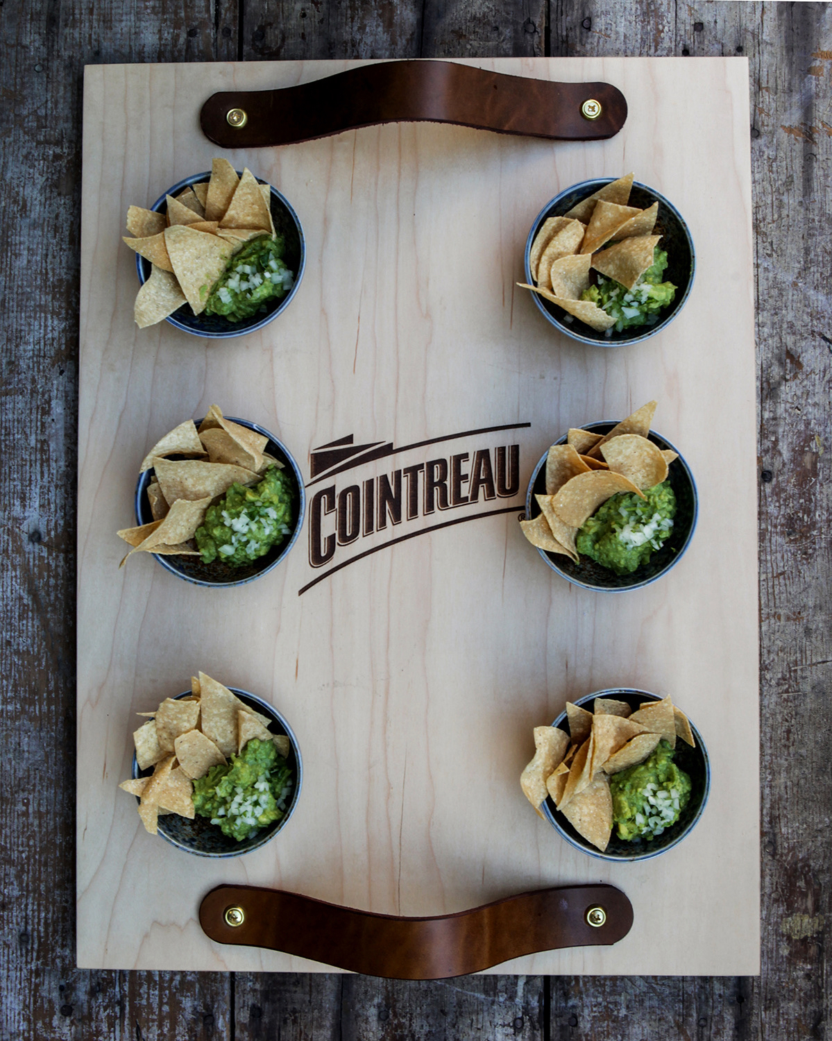 Cointreau-branded wooden board with guacamole and tortilla chips in six ceramic bowls