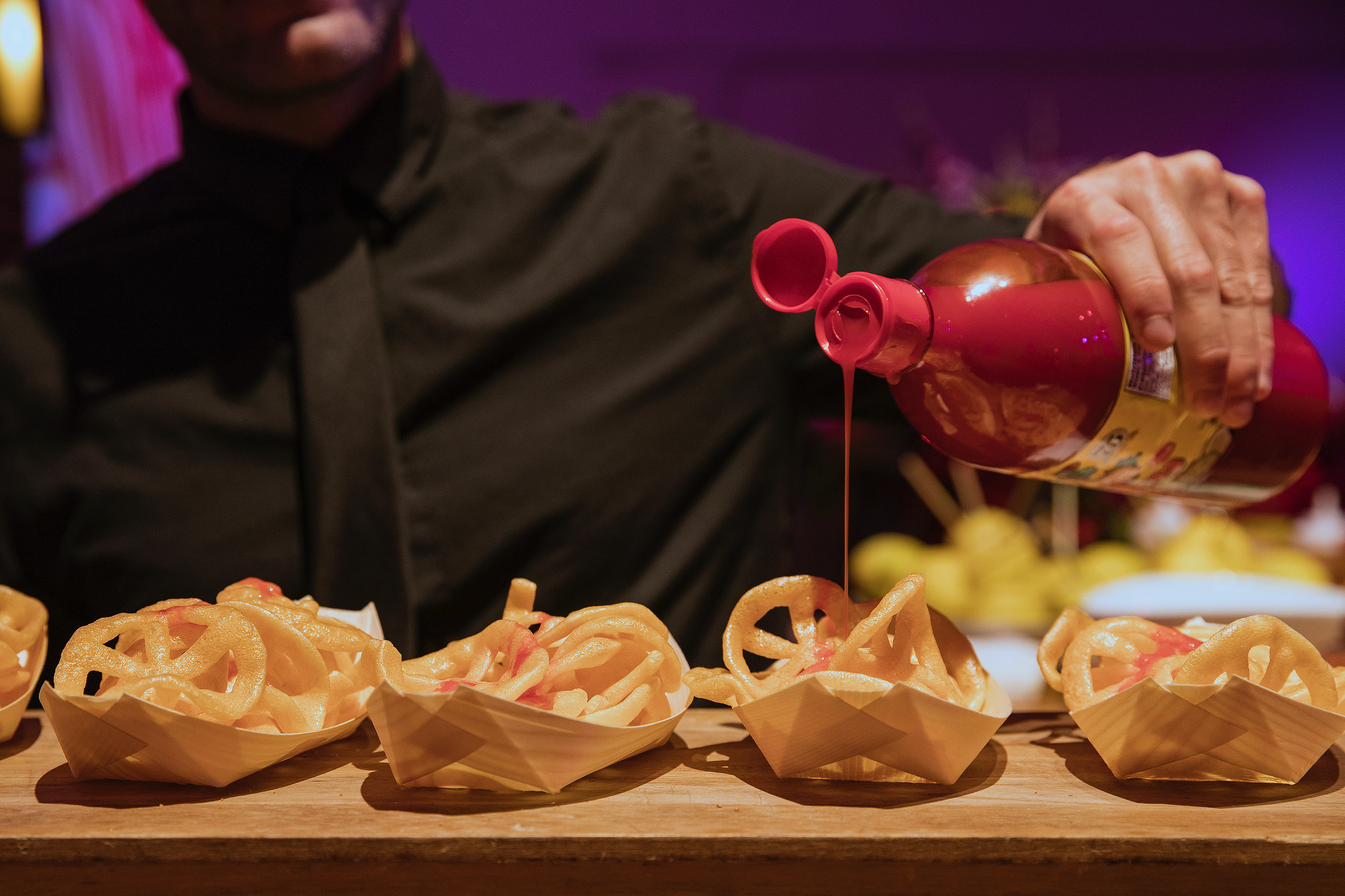 Catering professional drizzling red sauce onto golden fried snacks in wooden trays