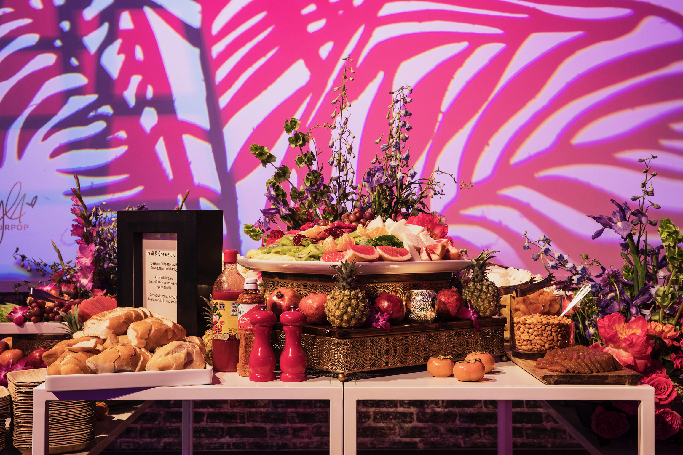 Lavish fruit and cheese station on an ornate gold stand with a vibrant projection backdrop