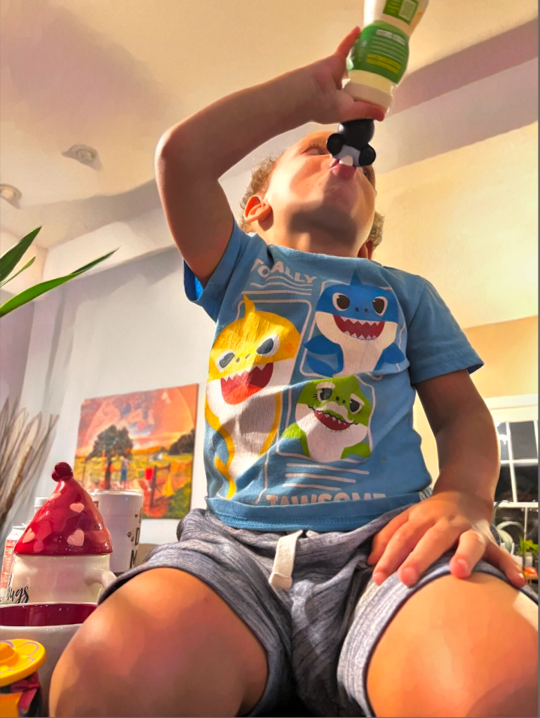 A boy in a Baby Shark t-shirt drinking from a small object